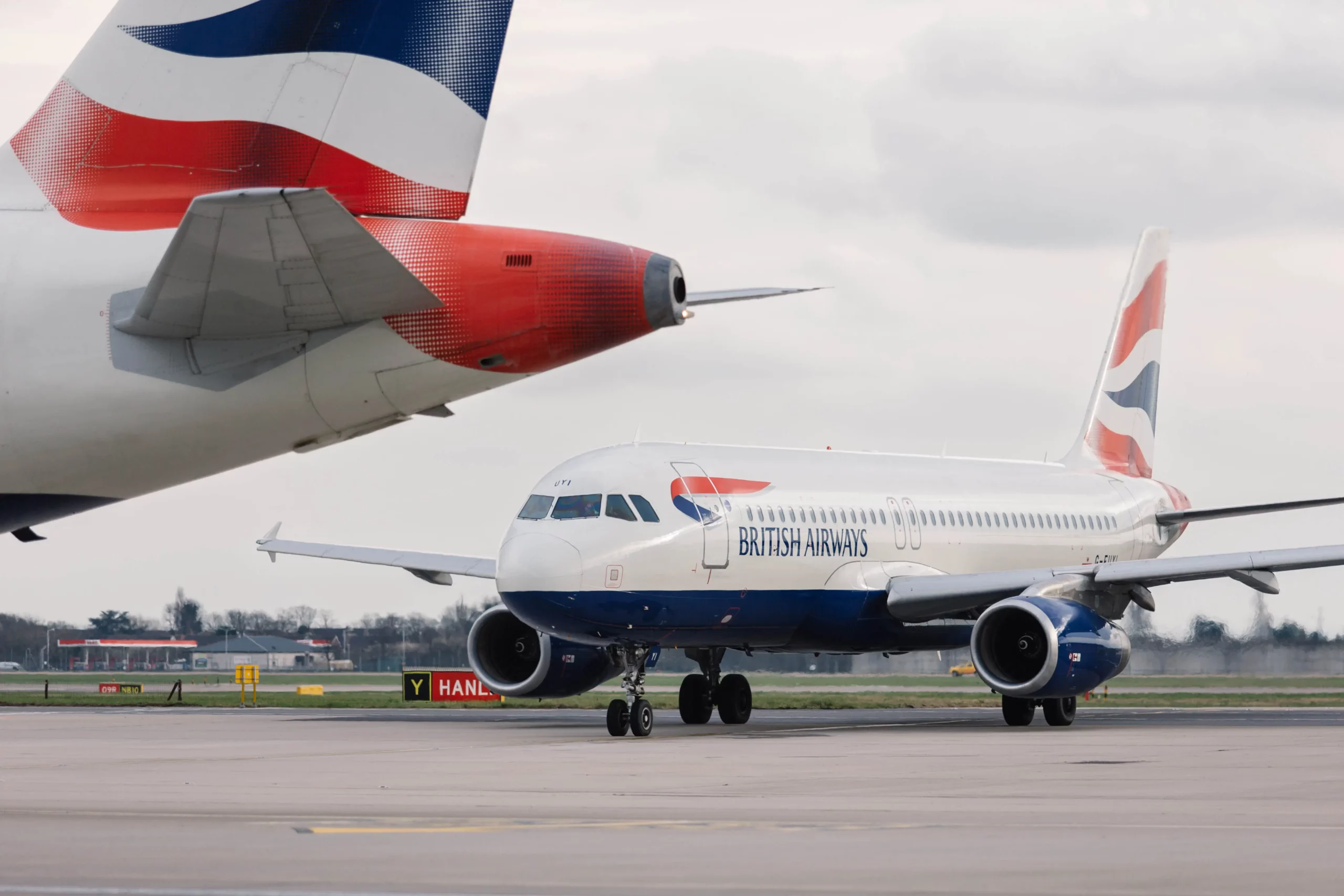 Photograph of a British Airways plane in the background, and the tail of a second British Airways plane in the foreground