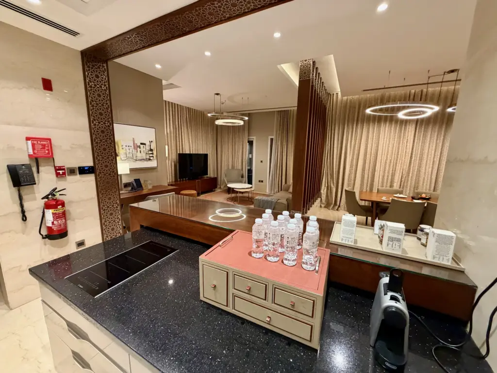 A photograph showing a kitchen inside the Al Messila resort, with the living space and dining space in the background. 