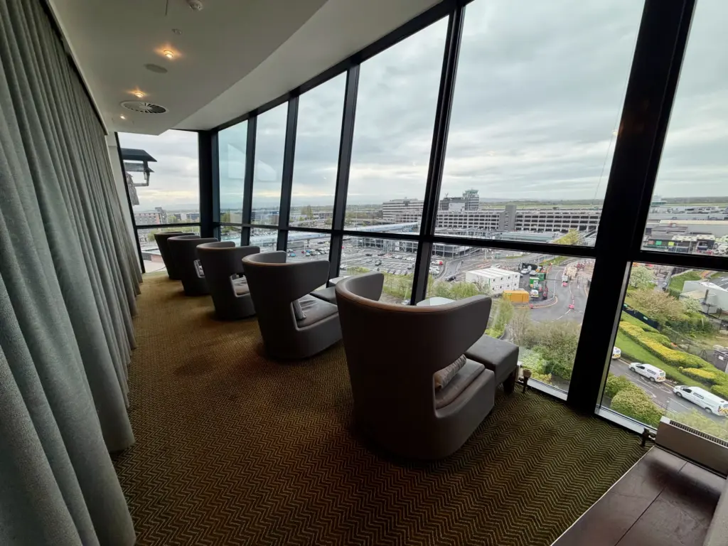 Cozy airport lounge with high-backed chairs facing large windows and a cityscape view outside.