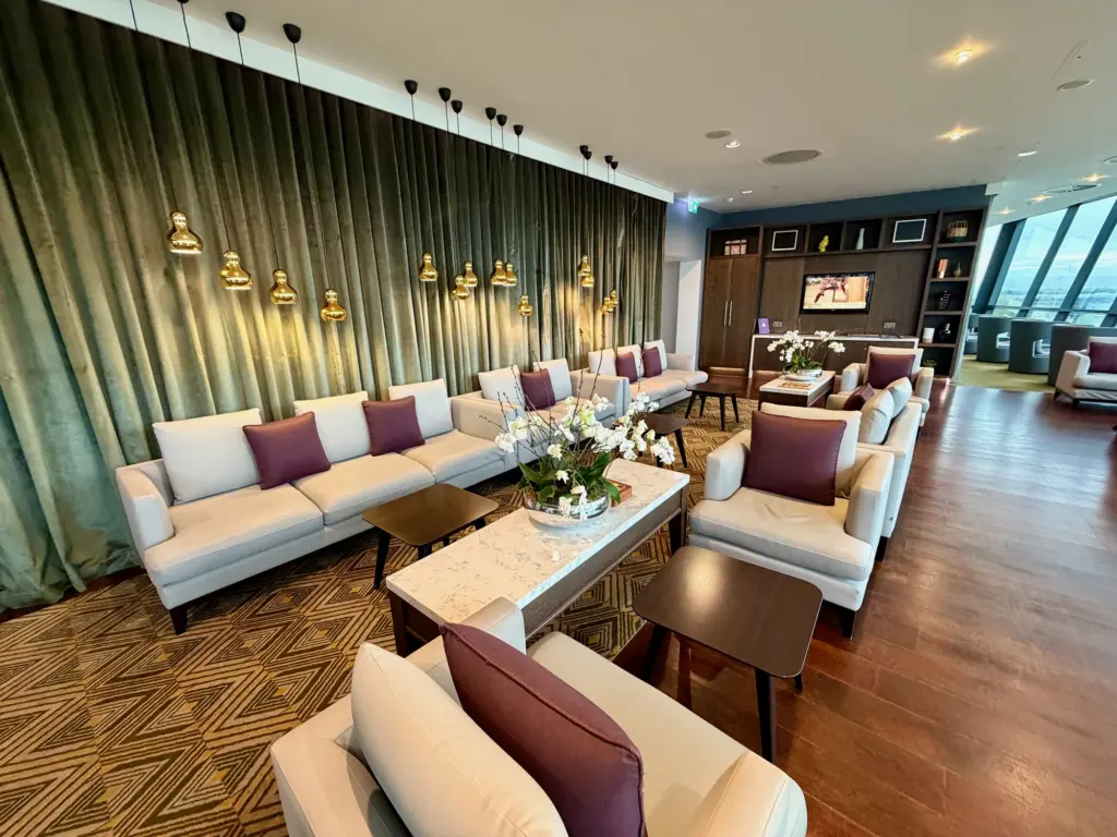 Luxurious hotel lounge with white sofas, purple cushions, marble coffee tables, and gold pendant lights along green velvet curtains.