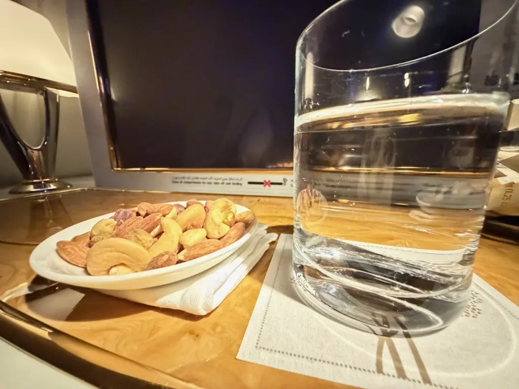 A bowl of warmed nuts and a glass of water before take off Photograph of a welcome drink and warmed nuts on an Emirates flight